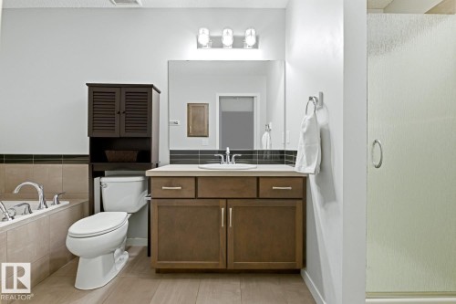 Bathroom featuring a wood-finish vanity with an integrated sink, a rectangular mirror, and a three-light fixture - 17844 61 Street, Edmonton, AB 