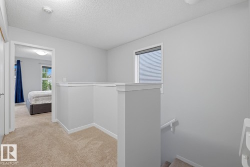 Carpeted hallway featuring a painted railing, neutral wall finishes, a recessed window, and overhead lighting - 17844 61 Street, Edmonton, AB 