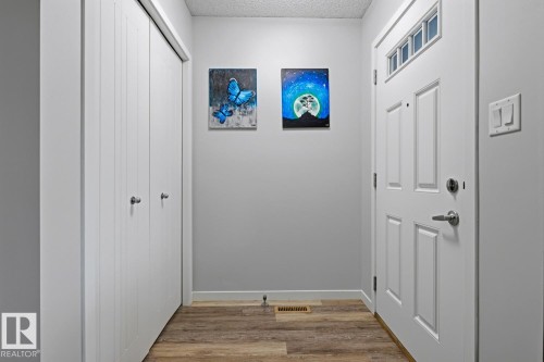 Entryway featuring wood-finish flooring, a white paneled door with transom windows, and a built-in closet with bifold doors - 17844 61 Street, Edmonton, AB 