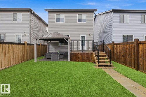 Rear exterior featuring a spacious green lawn, a wooden privacy fence, and a multi-level deck with a built-in gazebo - 17844 61 Street, Edmonton, AB 