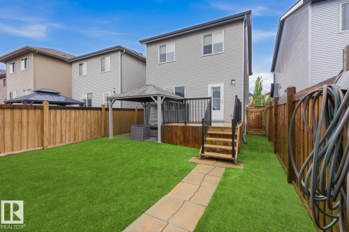 Expansive backyard featuring a lush green lawn, full privacy fencing, a wooden deck with black railings, and a stone paver pathway - 17844 61 Street, Edmonton, AB 