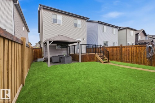 Expansive fenced backyard featuring a substantial wooden deck with black railings, a dedicated gazebo area, and a paved walkway - 17844 61 Street, Edmonton, AB 