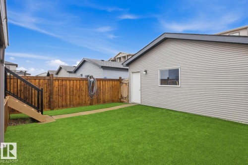 Expansive fenced backyard featuring artificial turf, a concrete pathway, and a detached garage with horizontal siding - 17844 61 Street, Edmonton, AB 