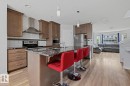 Modern kitchen with an island featuring a dark speckled countertop, stainless steel appliances, wood-finish cabinetry, white subway tile backsplash, and wood-finish flooring - 17844 61 Street, Edmonton, AB 