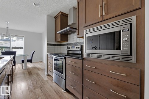 Kitchen featuring wood-finish flooring, dark wood cabinetry, stainless steel appliances, dark countertops, and a subway tile backsplash - 17844 61 Street, Edmonton, AB 