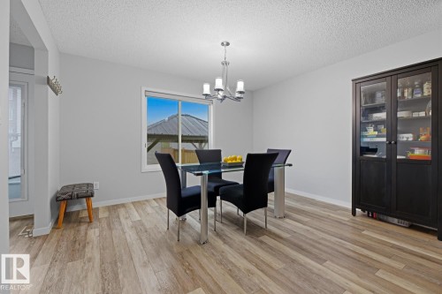 Light wood-finish flooring throughout, complemented by a contemporary chandelier with frosted glass shades - 17844 61 Street, Edmonton, AB 