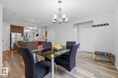 Open-concept main level featuring wood-finish flooring, a kitchen island with a granite-style countertop, stainless steel refrigerator, and recessed lighting - 17844 61 Street, Edmonton, AB 