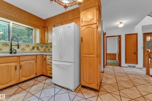 Kitchen featuring wood cabinetry, a white refrigerator, a black gooseneck faucet, and a window with exterior views - 10819 54 Avenue, Edmonton, AB 