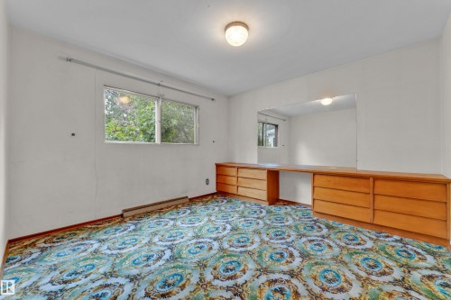 Room featuring a window with exterior foliage, patterned carpet flooring, and a built-in wood-finish vanity with drawer storage - 10819 54 Avenue, Edmonton, AB 