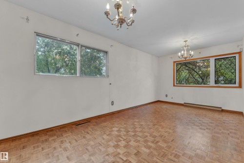 Spacious room featuring parquet wood flooring, two ornate chandeliers, and multiple windows providing natural illumination - 10819 54 Avenue, Edmonton, AB 