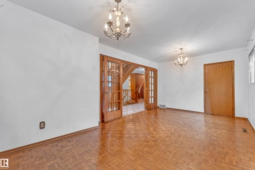 Spacious room with parquet wood-finish flooring, white walls, and two ornate chandeliers - 10819 54 Avenue, Edmonton, AB 