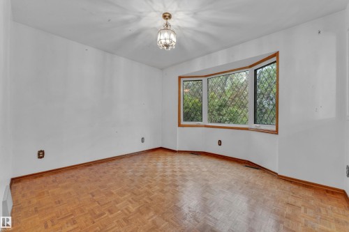 Room featuring a prominent bay window with diamond-patterned muntins, wood-finish flooring, and a central ceiling light fixture - 10819 54 Avenue, Edmonton, AB 