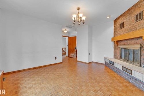 Living area featuring a brick fireplace with a wood mantle, a tile hearth, and wood-finish parquet flooring - 10819 54 Avenue, Edmonton, AB 