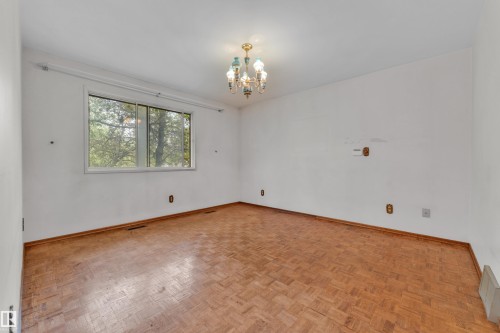 Spacious room featuring wood-finish parquet flooring, white walls, and a large window providing ample natural light - 10819 54 Avenue, Edmonton, AB 