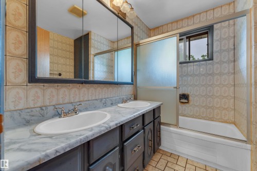 Bathroom vanity featuring dual inset sinks, a marbled countertop, and dark cabinetry with silver hardware - 10819 54 Avenue, Edmonton, AB 