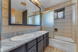 Bathroom vanity featuring dual inset sinks, a marbled countertop, and dark cabinetry with silver hardware - 