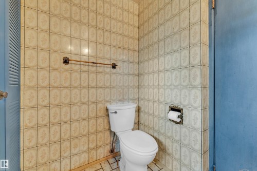 Bathroom featuring floor-to-ceiling decorative wall tiling and a white toilet - 10819 54 Avenue, Edmonton, AB 