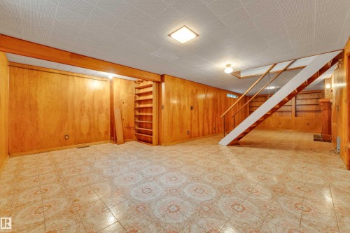 Spacious lower-level room featuring patterned tile flooring, wood paneling, and a built-in bookshelf - 10819 54 Avenue, Edmonton, AB 