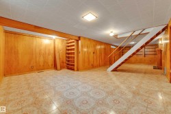Spacious lower-level room featuring patterned tile flooring, wood paneling, and a built-in bookshelf - 
