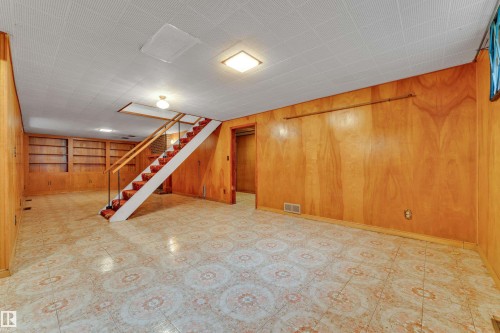 Spacious lower level featuring wood-finish wall paneling, patterned floor tiling, and a staircase with a wood handrail and metal balusters - 10819 54 Avenue, Edmonton, AB 