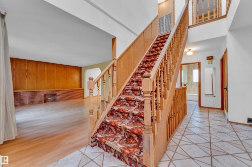 Entry foyer featuring geometric floor tiling, a wooden staircase with patterned runner, and a double-height ceiling - 10819 54 Avenue, Edmonton, AB 