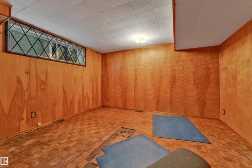 Room featuring wood-paneled walls, a drop ceiling, and parquet wood-finish flooring - 10819 54 Avenue, Edmonton, AB 