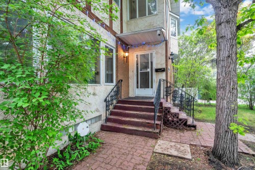 Brick and textured stucco facade featuring a covered entry, wrought iron railings, red paver stone walkway, and mature trees - 10819 54 Avenue, Edmonton, AB 