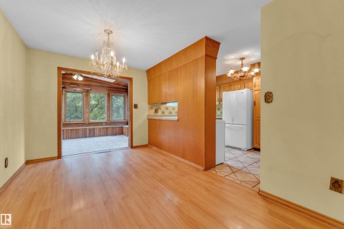 Open concept living space featuring wood-finish flooring, a crystal chandelier, and a sunroom with large windows and wood paneling - 10819 54 Avenue, Edmonton, AB 