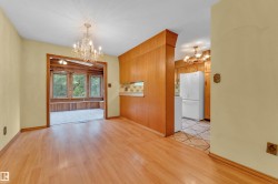 Open concept living space featuring wood-finish flooring, a crystal chandelier, and a sunroom with large windows and wood paneling - 