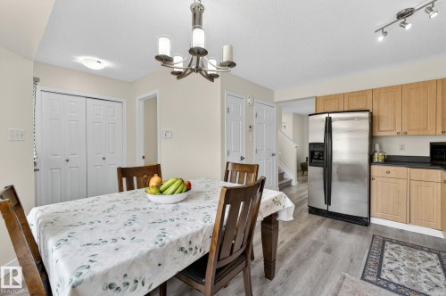 Open concept dining area with wood-finish flooring, a contemporary chandelier, light wood cabinetry, and stainless steel appliances - 21244 90 Avenue, Edmonton, AB 