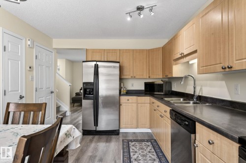 Kitchen featuring light wood-finish cabinetry, dark countertops, a stainless steel side-by-side refrigerator, a stainless steel dishwasher, and wood-finish flooring - 21244 90 Avenue, Edmonton, AB 