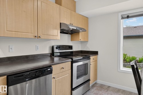 Kitchen featuring light wood-finish cabinetry, stainless steel appliances, dark countertops, and a window with exterior landscaping - 21244 90 Avenue, Edmonton, AB 
