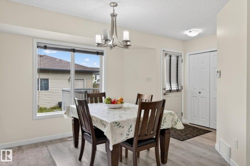 Dining space featuring wood-finish flooring, a contemporary chandelier, and a large window - 21244 90 Avenue, Edmonton, AB 