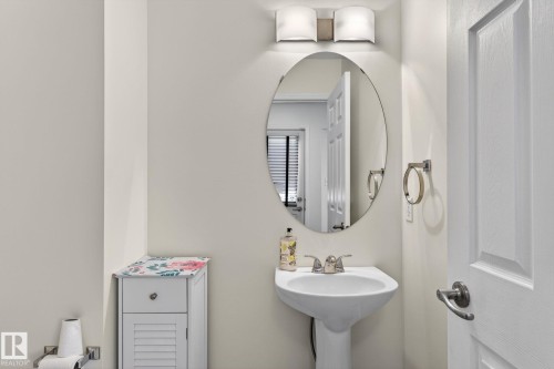 Pedestal sink with chrome faucet, an oval wall-mounted mirror, and a two-light vanity fixture - 21244 90 Avenue, Edmonton, AB 