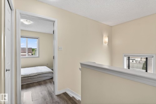 Hallway featuring wood-finish flooring, a wall-mounted sconce, and a window with blinds - 21244 90 Avenue, Edmonton, AB 