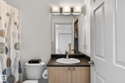 Bathroom vanity featuring a light wood-finish cabinet with double doors, a white oval sink, and a dark countertop - 21244 90 Avenue, Edmonton, AB 