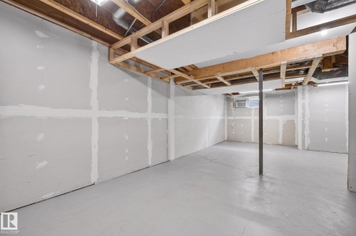 Unfinished basement space featuring exposed wood joists and subfloor, drywall-ready walls, painted concrete flooring, and a single support column - 21244 90 Avenue, Edmonton, AB 