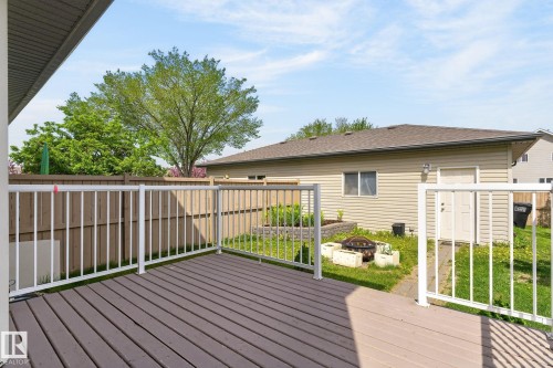 Expansive outdoor wood-finish deck with white railings, a separate fenced yard area, a raised garden bed, and a detached structure with light-colored siding - 21244 90 Avenue, Edmonton, AB 