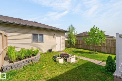 Expansive backyard featuring a stone block retaining wall with plantings, a paved pathway, a full-height wood fence, and a neutral-toned vinyl-sided exterior - 21244 90 Avenue, Edmonton, AB 