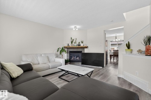 Living room featuring a gas fireplace with a stone surround and wood-finish mantel, wood-finish flooring, and recessed lighting - 21244 90 Avenue, Edmonton, AB 