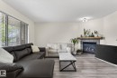 Spacious living area featuring wood-finish flooring, a corner fireplace with stone surround and wooden mantel, and a large window with horizontal blinds - 21244 90 Avenue, Edmonton, AB 