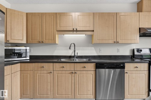 Kitchen featuring light wood cabinetry, dark countertops, a double basin sink with a gooseneck faucet, and a stainless steel dishwasher - 21244 90 Avenue, Edmonton, AB 
