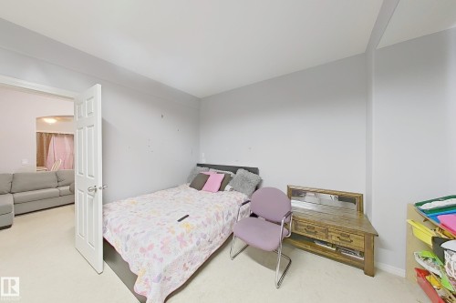 Bedroom space with light gray walls and plush carpeting, featuring a white door frame and an arched entryway to an adjacent area - 41 5102 30 Avenue, Beaumont, AB 