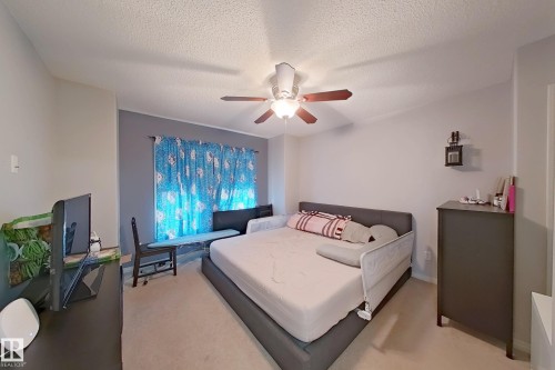 Carpeted room featuring a ceiling fan with light fixture and a window with blue patterned curtains - 41 5102 30 Avenue, Beaumont, AB 