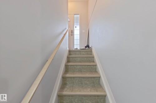 Staircase featuring tiled treads, light-toned risers, a natural wood handrail, and a frosted glass-paneled entry door - 41 5102 30 Avenue, Beaumont, AB 