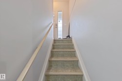 Staircase featuring tiled treads, light-toned risers, a natural wood handrail, and a frosted glass-paneled entry door - 