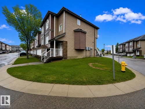 Corner unit townhome featuring tan siding, dark brown trim, and a white railing entry - 41 5102 30 Avenue, Beaumont, AB 