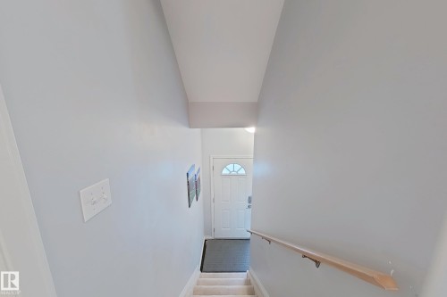 Carpeted staircase descending towards a front entry door with a decorative half-moon window - 41 5102 30 Avenue, Beaumont, AB 