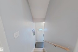 Carpeted staircase descending towards a front entry door with a decorative half-moon window - 