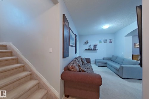 Carpeted staircase with white trim, featuring a living area with wall-mounted shelving and an arched doorway - 41 5102 30 Avenue, Beaumont, AB 